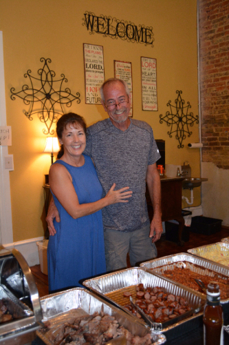 Image of a woman and a man standing in front of a table containing food.