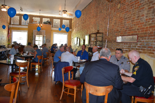 Image of several people sitting around multiple tables enjoying a meal.
