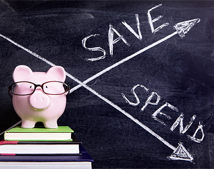 Pink piggy bank with glasses standing on books next to a blackboard with simple spend and save message. Sharp focus on the piggy bank with blackboard slightly blurred.
** Note: Soft Focus at 100%, best at smaller sizes