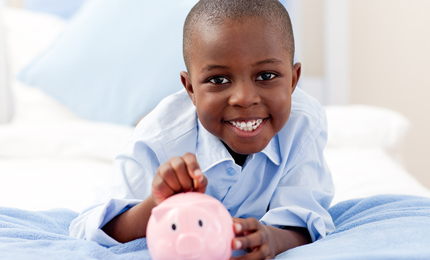Young boy smiling at the camera while putting money into his piggy bank