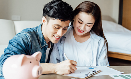 A young asian couple is sitting on a carpet using a computer