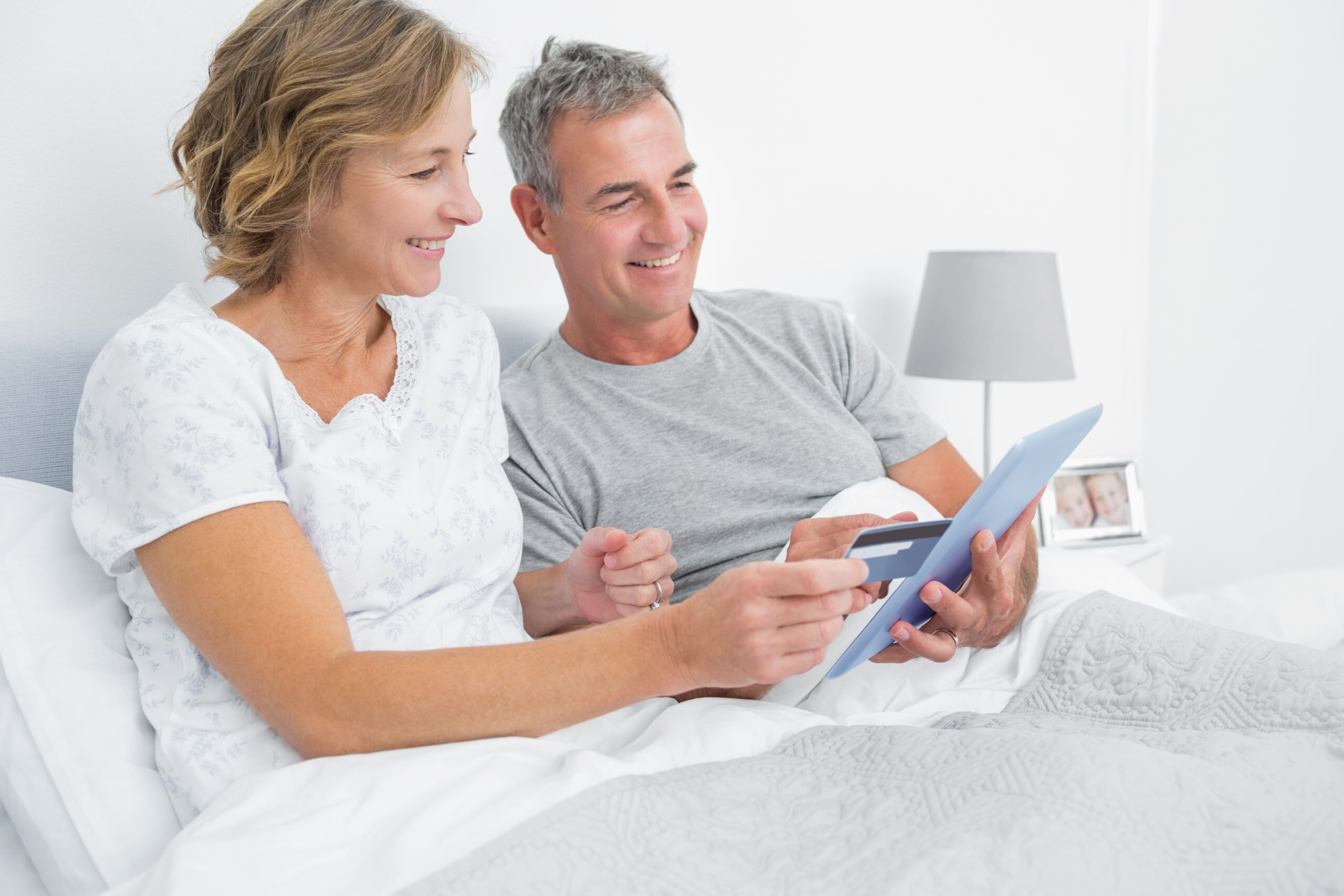 Cheerful couple using their tablet pc to buy online at home in bedroom